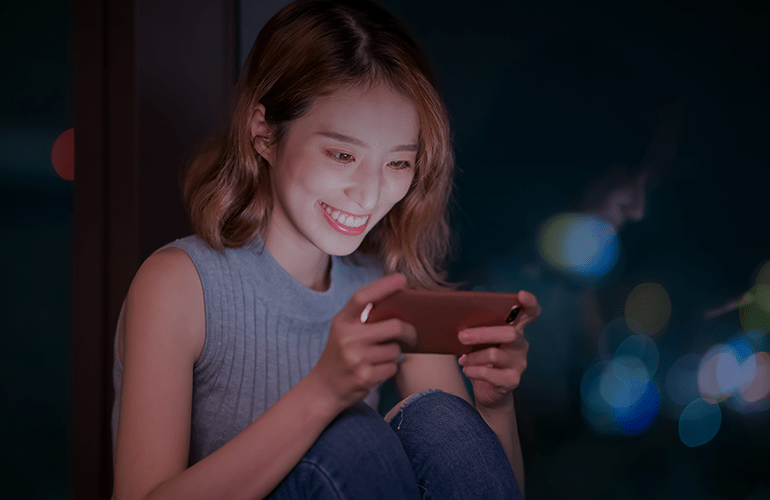 Young woman smiling while playing a mobile game at night on her smartphone