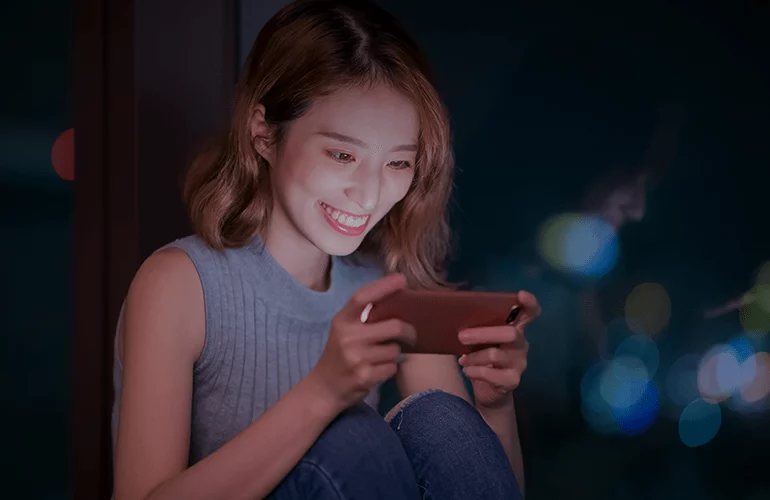 Young woman smiling while playing a mobile game at night on her smartphone