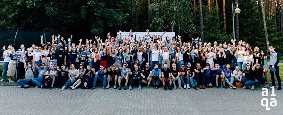 a1qa team group photo outdoors at summer professional conference, many raising hands
