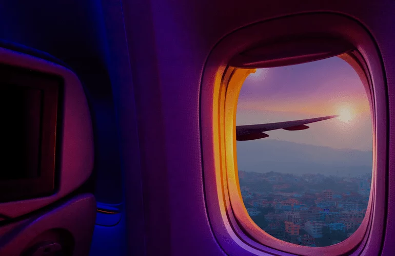 Airplane window view of sunset over city, suggesting travel reporting perspective