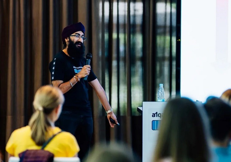 Speaker presenting at an a1qa event, addressing an audience with microphone near podium
