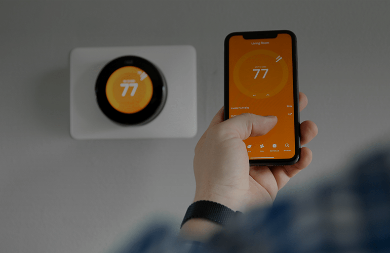 Hand using smartphone app to control smart home thermostat set to 77