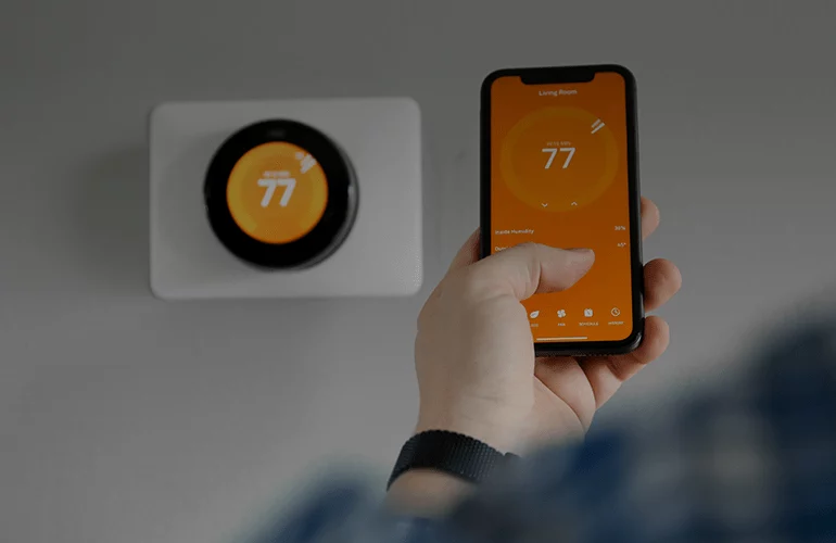 Hand using smartphone app to control smart home thermostat set to 77