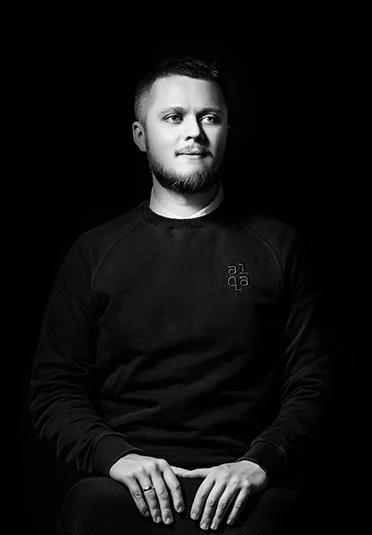 Black-and-white portrait of a1qa team member seated in a dark sweatshirt with a1qa logo