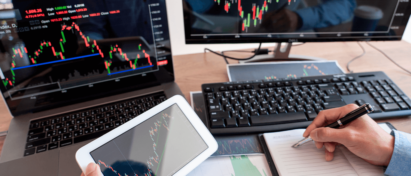 Analyst reviewing trading charts on multiple devices while taking notes at a desk
