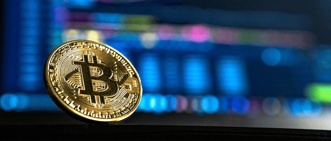 Bitcoin coin in front of blurred digital market charts representing blockchain technology testing