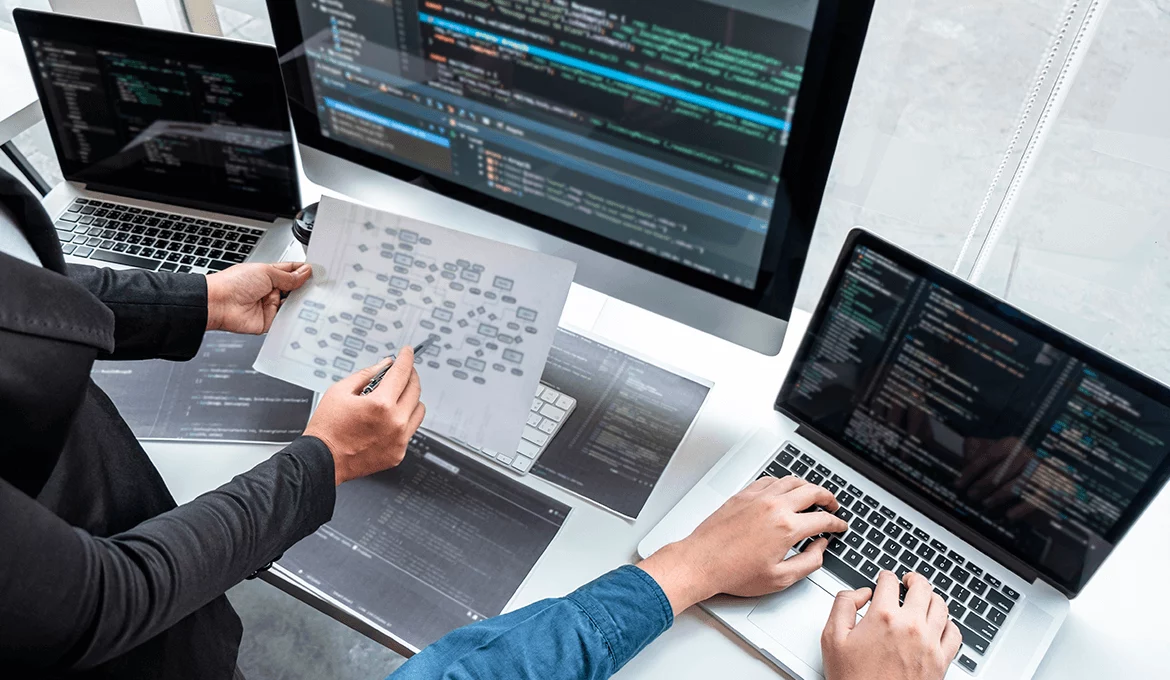 Engineers review system validation flowchart and code across multiple screens and laptops