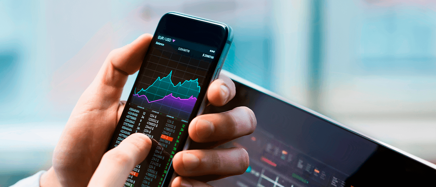 Hand using smartphone with EUR/USD market charts and trading dashboard on screen
