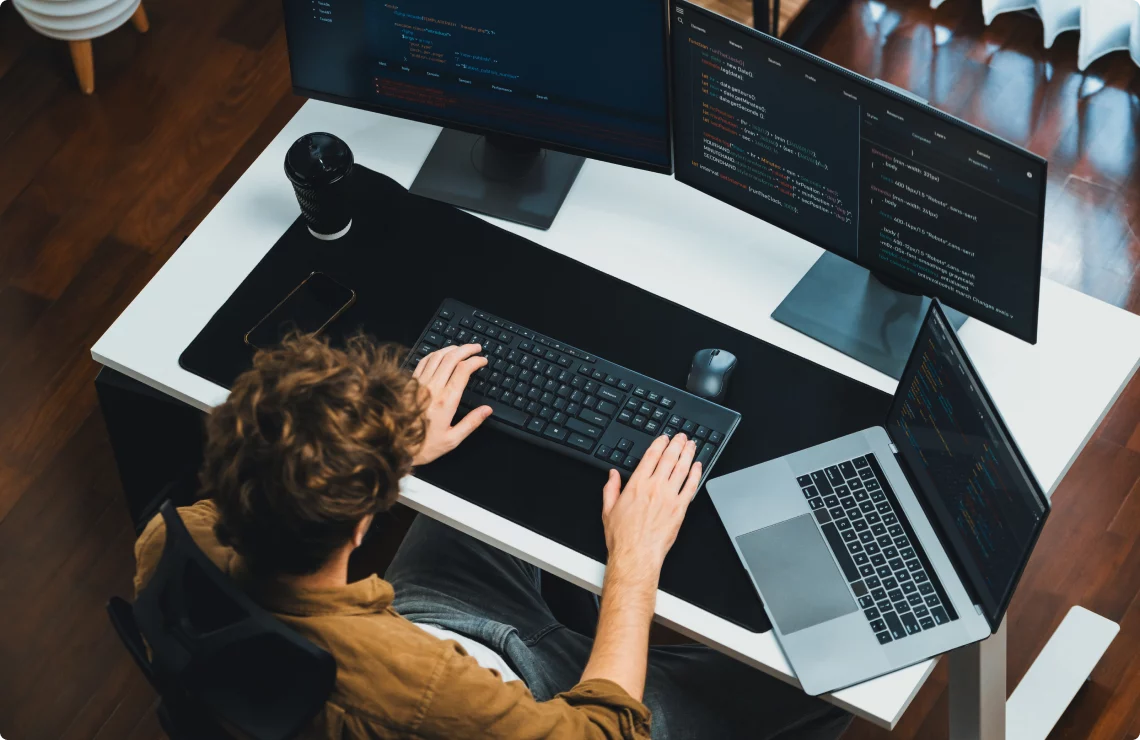 Developer working at multi-monitor workstation with code, representing software performance testing services