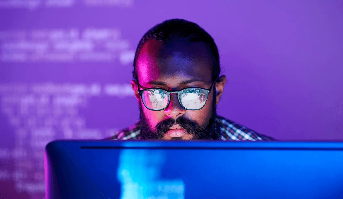 Software tester analyzing web service performance on a computer in a low-light workspace