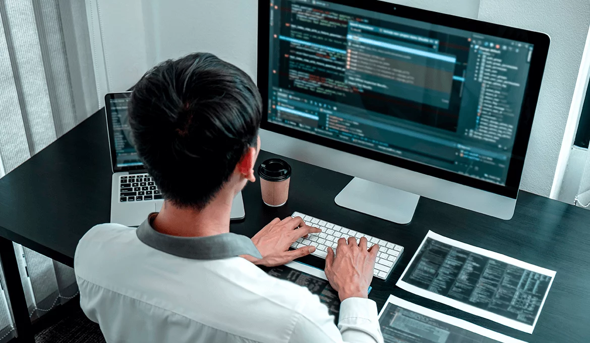 Software tester reviewing application code and functional test results at a workstation