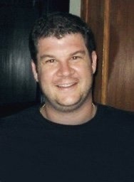 Headshot of a smiling man in a black shirt indoors