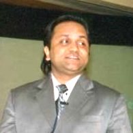 Man in suit speaking at an event, looking to the side