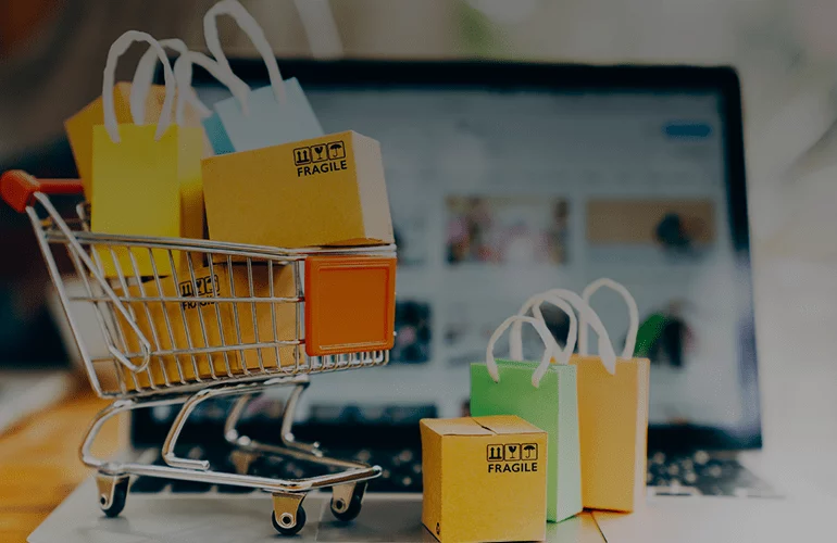 Mini shopping cart with bags and FRAGILE boxes in front of an online store screen