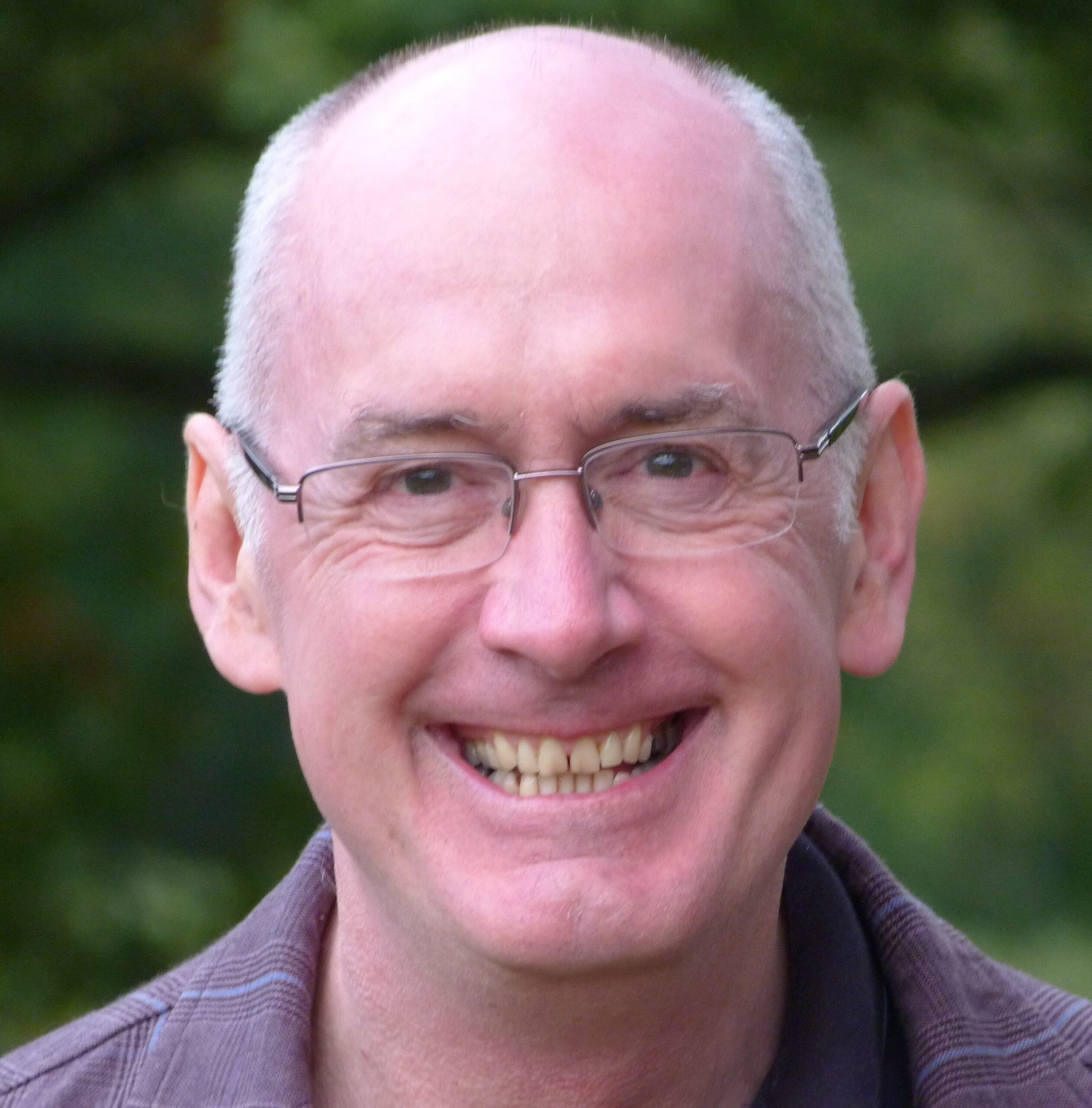 Portrait of James Christie smiling outdoors and wearing glasses