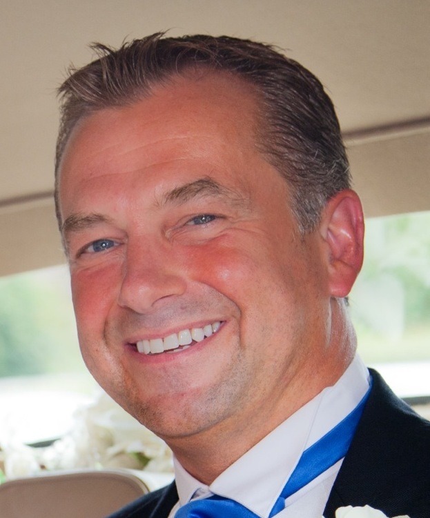 Portrait of Lloyd Roden smiling in a suit and blue tie