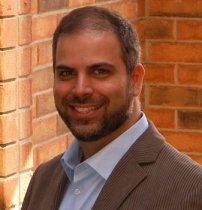 Portrait of a smiling bearded man in business attire against a brick wall