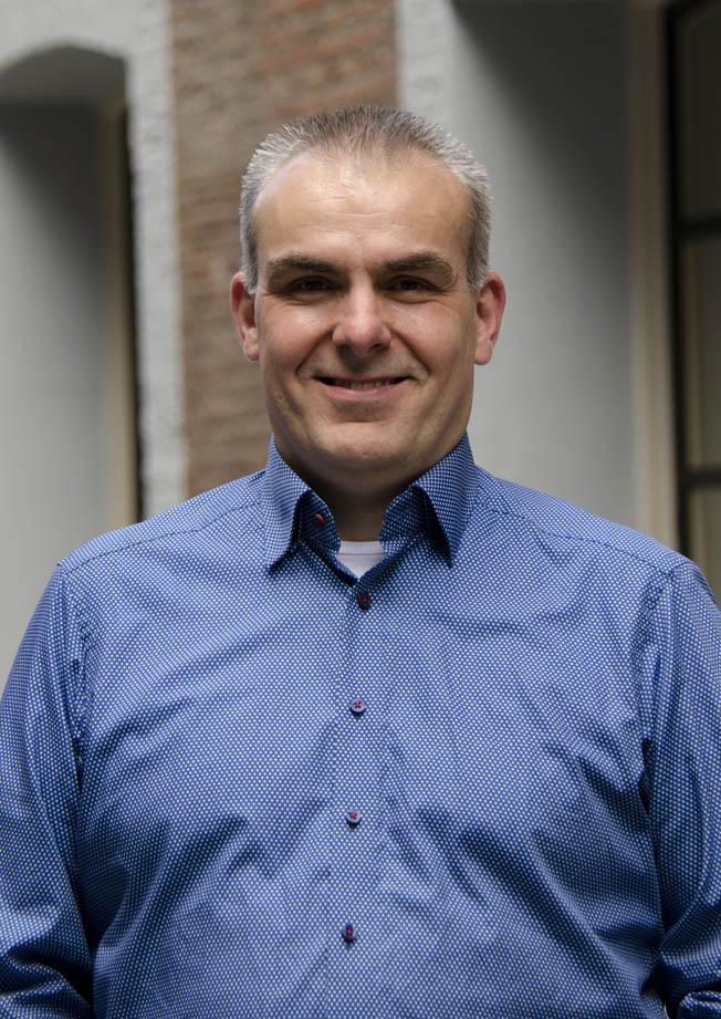 Portrait of a smiling man in a blue patterned shirt in an office setting