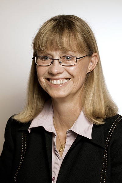 Professional headshot of a smiling woman wearing glasses and a business suit