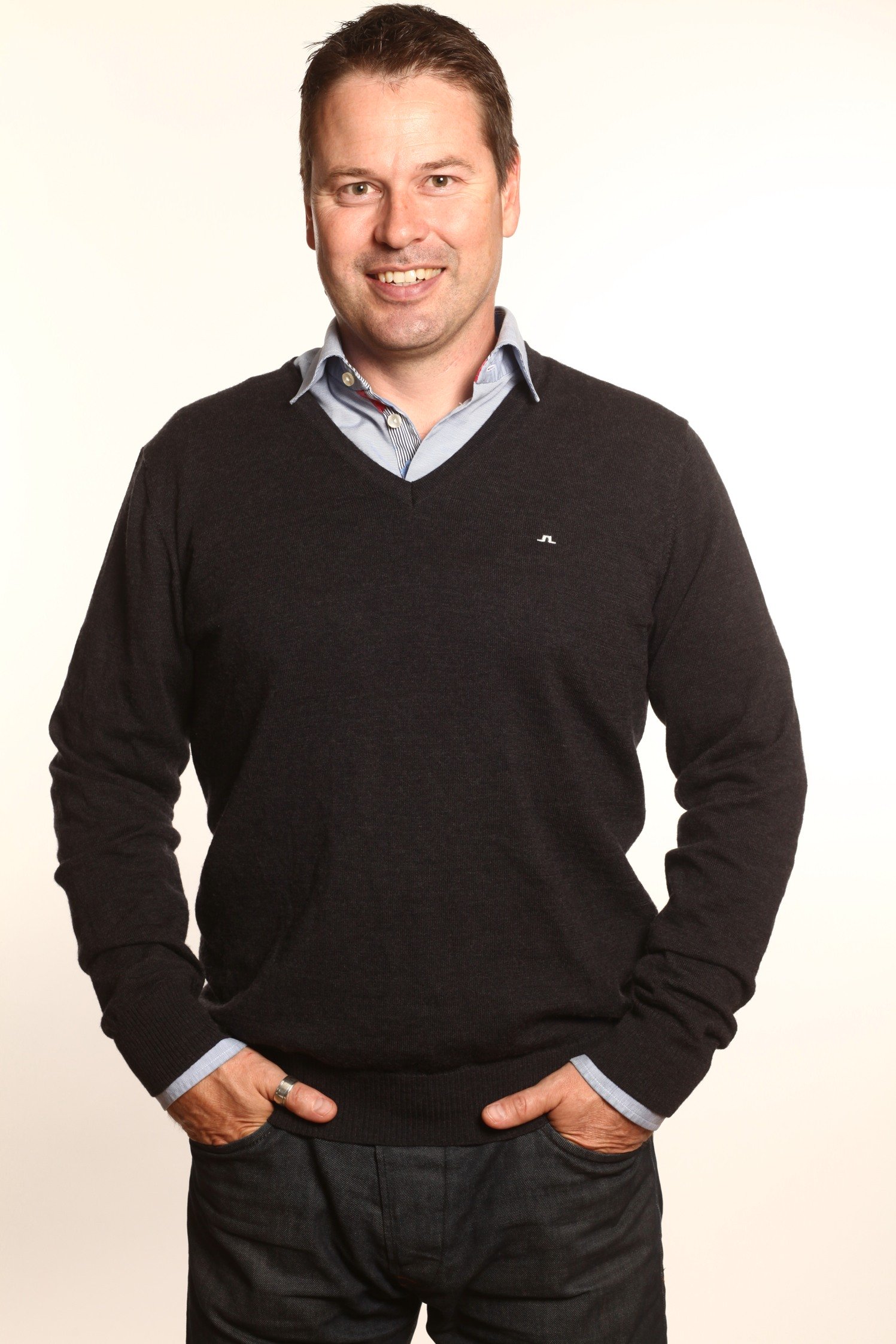 Smiling man in sweater and collared shirt standing with hands in pockets