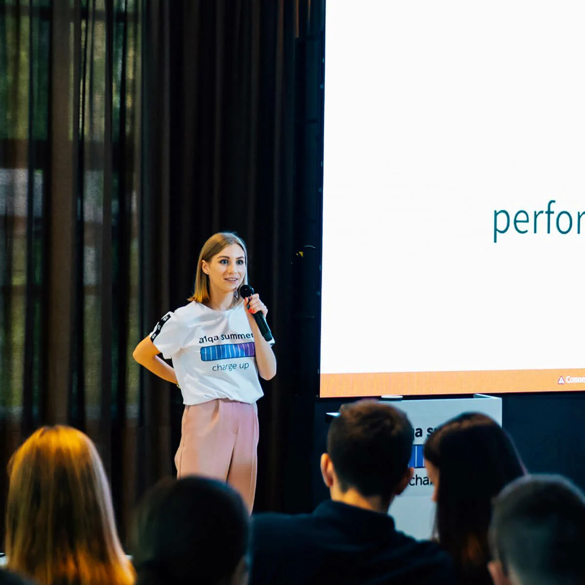 Speaker presenting at a1qa summer charge up event to an audience beside projection screen
