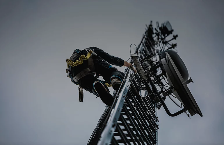 Technician climbing a communications tower, illustrating work at height and complex infrastructure