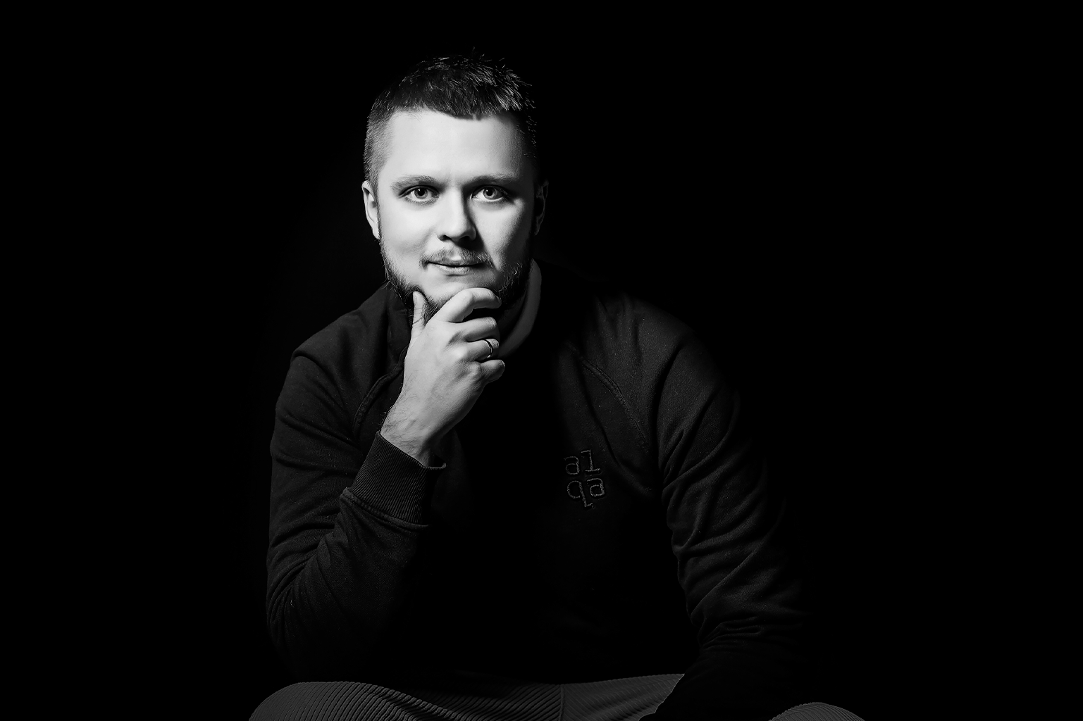 Black-and-white portrait of a man in an a1qa sweatshirt, hand on chin
