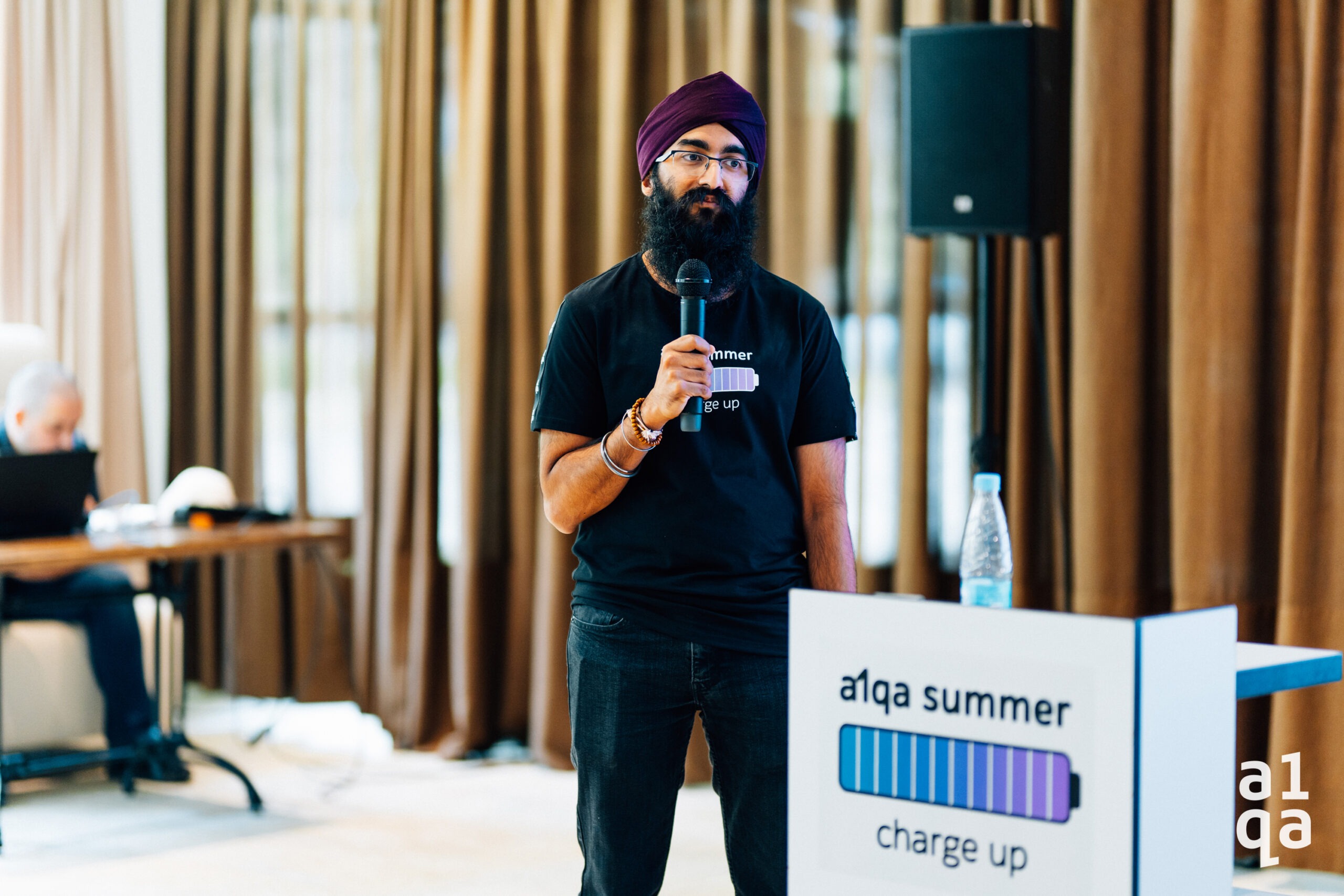 Speaker holding microphone beside a1qa summer charge up podium at a conference