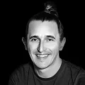 Black-and-white headshot of a smiling man with a top knot hairstyle